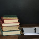 pile of books beside white printer paper and black ballpoint pen